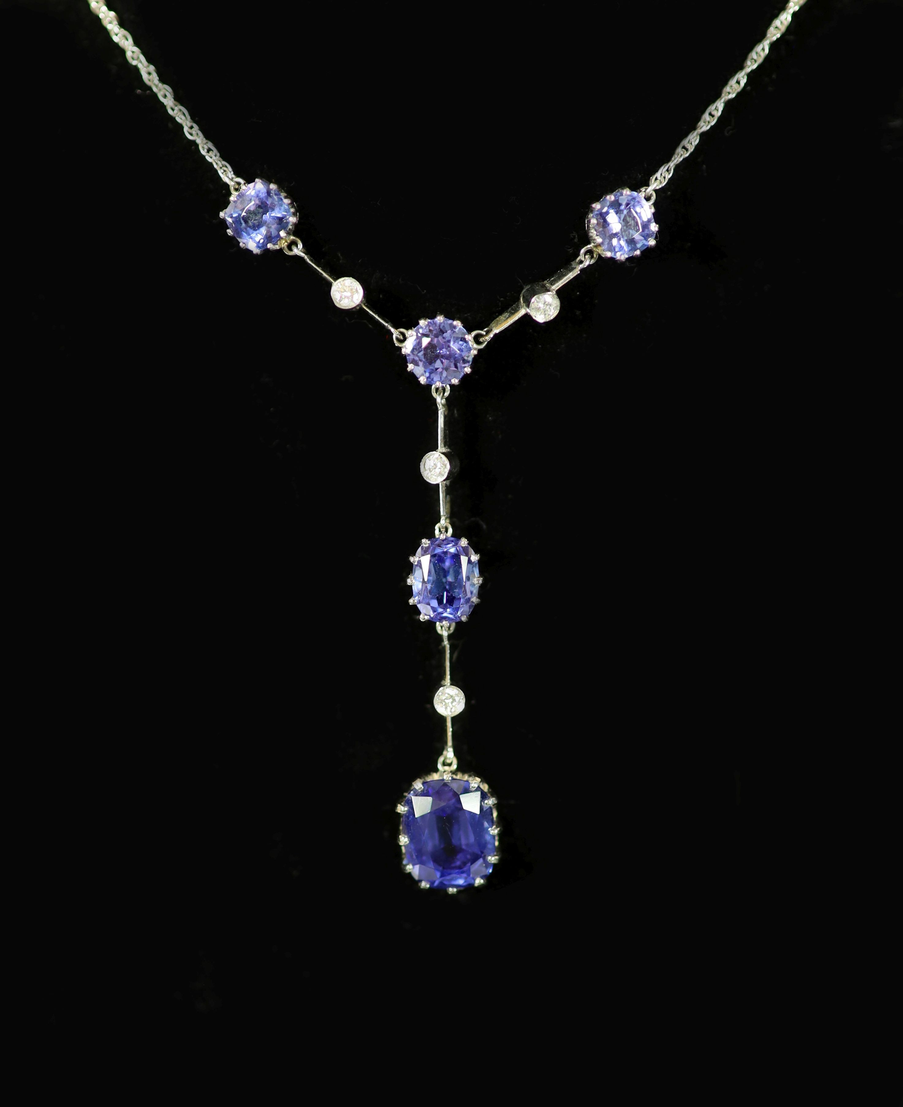 A modern platinum, five stone tanzanite and four small round cut diamond set drop pendant necklace